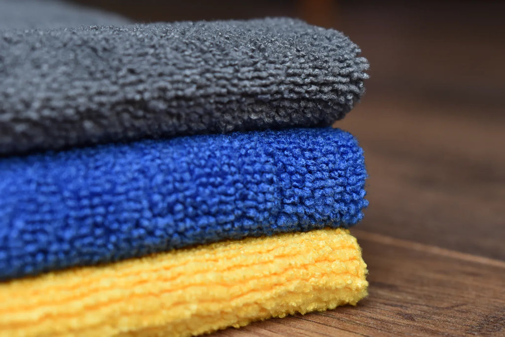 KHEMIA PLUS The Daily premium 365 GSM edgeless microfiber towels stacked in three colors - dark grey, royal blue, and golden yellow showing terry weave texture