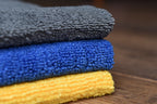KHEMIA PLUS The Daily premium 365 GSM edgeless microfiber towels stacked in three colors - dark grey, royal blue, and golden yellow showing terry weave texture