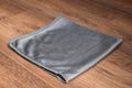 Khemia Plus Carbon Glass microfiber towel folded on wood surface, gray weave with stitched edges