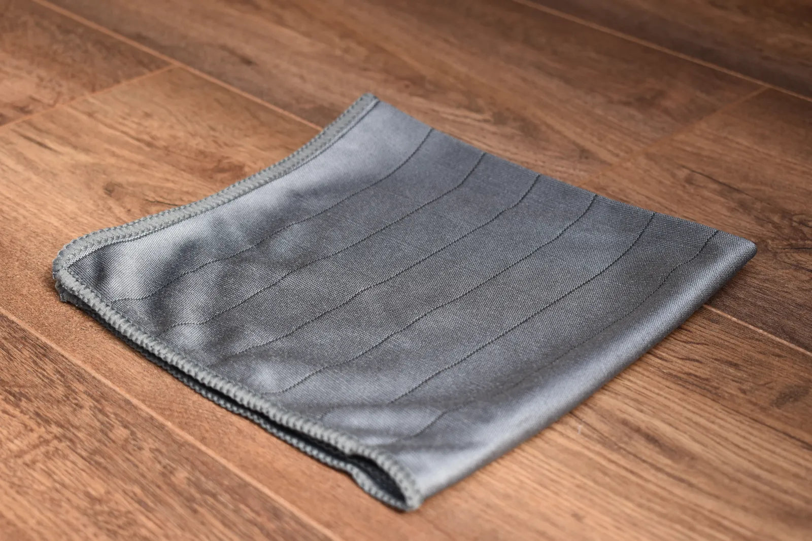 Khemia Plus Carbon Glass microfiber towel folded on wood surface, gray weave with stitched edges